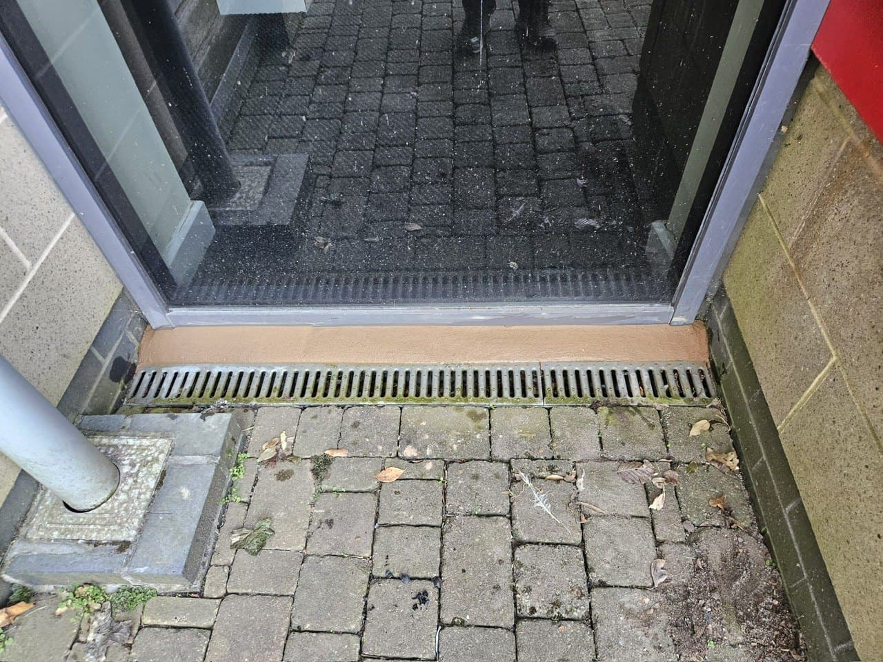 Sealed threshold and drainage channel at a commercial shopfront entrance — waterproofing at ground level.