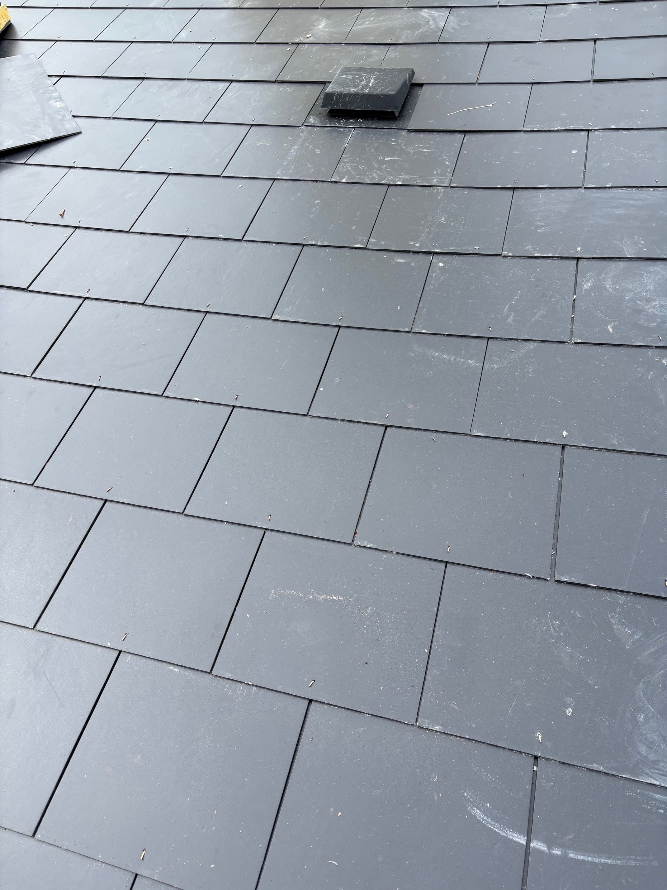 Finished new natural slate roof in clean even grid with single roof vent — recent re-roof in West Devon.