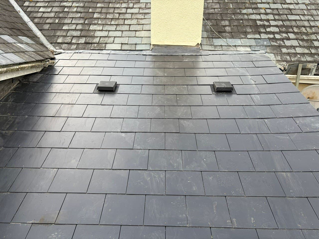 Finished natural slate roof installed by Mets Roofing Southwest on a Devon property — two vents and clean even courses against a yellow-render chimney.